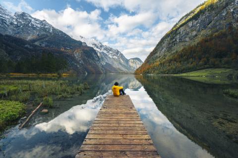 Man sitting on a wooden dock on Lake Königssee. Located in the heart of the Berchtesgaden National Park and bordered by the eastern side of Mount Watzmann.