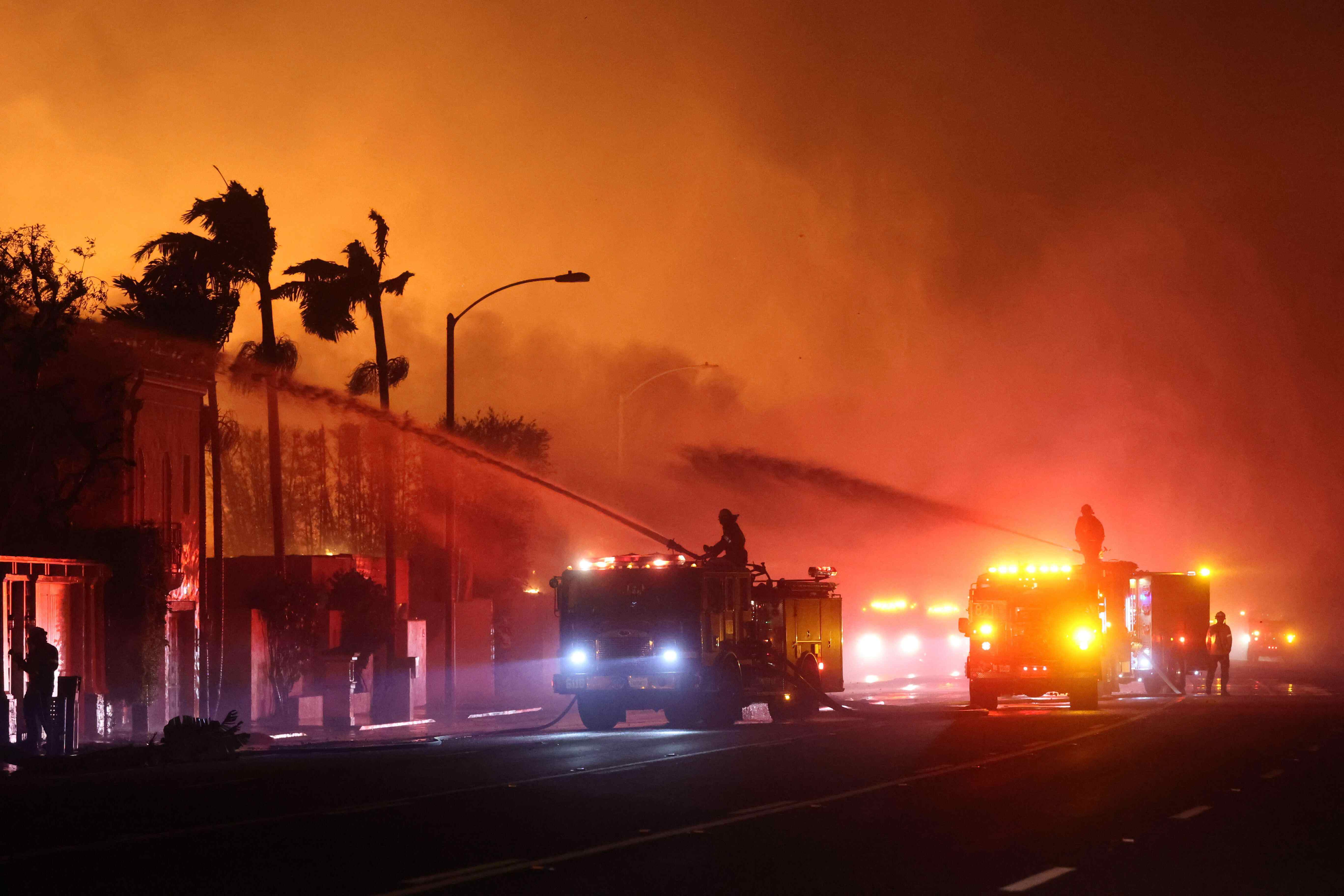 Firefighters spray water on burning structures to contain the rapid spread of the Palisades Fire in Los Angeles, California. 