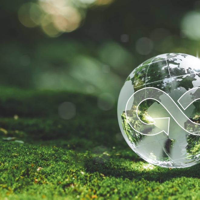 Transparent Earth with a circular economy symbol inside it sitting on the grass.