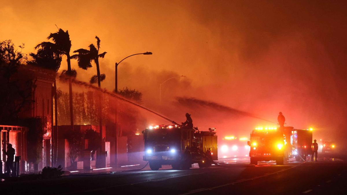 Firefighters spray water on burning structures to contain the rapid spread of the Palisades Fire in Los Angeles, California. 